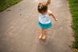 © Adam Hester - A toddler aged girl playing hopscotch outside in a park.