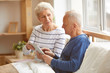 Portrait of modern senior couple using digital tablet sitting on bed in sunlight, copy space