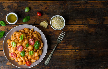 Wall Mural - Conchiglie abissine rigate pasta with tomato sauce, cherry tomatoes, and basil against dark wooden background