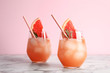 Glasses of grapefruit cocktail on table against color background