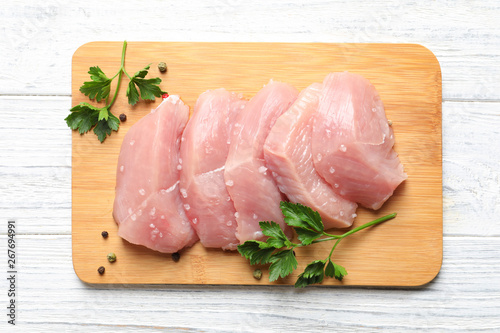 Cuadros en Lienzo Board with cut raw turkey fillet and parsley on white wooden background, top vie