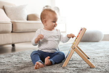 Cute baby playing with abacus on floor in room