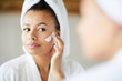 © Seventyfour - Head and shoulders portrait of  beautiful Mixed-Race woman applying face cream during morning routine, copy space