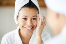 Head And Shoulders Portrait Of  Smiling Mixed-Race Woman Applying Face Cream During Morning Routine, Copy Space