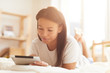 © Seventyfour - Portrait of beautiful Mixed-Race woman using digital tablet lying on bed lit by sunlight, copy space