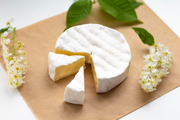 a camembert cheese wheel lying on a table among white flowers and green leaves, two pieces cut off