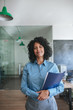 © mavoimages - Smiling young businesswoman standing in an office carrying files