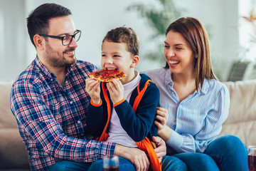 Portrait of happy family eating pizza while sitting on sofa at home