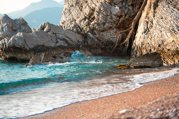 Beautiful sunny beach with blue waves, orange sand on seahore and cliffs.