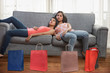 © IndiaPix - Two teenage girls lying exhausted on sofa at home after shopping with shopping bags on the floor