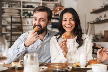 Sticker - Image of young couple eating together at table while having breakfast in kitchen at home