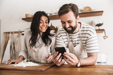 Sticker - Portrait of happy couple reading recipe while cooking pastry with flour and eggs in kitchen at home