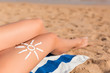 © sosiukin - Sun cream is drawn in sun shape on tanned woman's leg who is relaxing on the towel at the beach. Cancer care concept