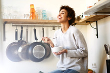 Happy Young Woman Eating Cereal From Bowl In Kitchen At Home