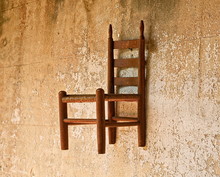 An Old Wooden Chair Hanging On A Brown Plaster Wall