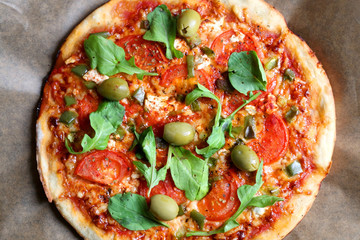 Homemade vegetarian pizza with tomato sauce, two types of cheese, tomatoes, peppers, arugula, olives and herbs. Top view.