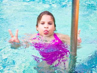 people, gesture and teens concept - happy smiling pretty teenage girl showing peace sign over blue water background, in swimming pool