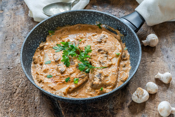 Pork chops in creamy cajun sauce with button mushrooms and parsley in a skillet