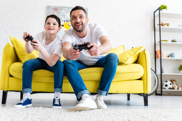 Wall Mural - excited father and son playing Video Game on couch in Living Room