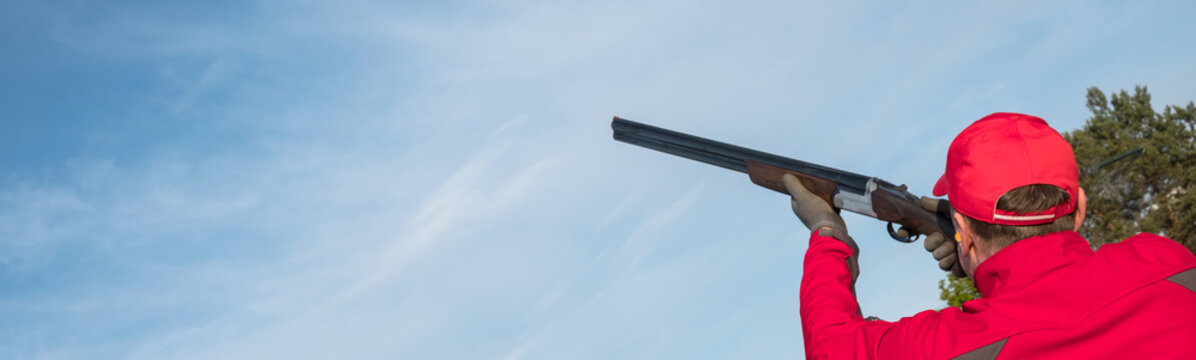 man shooting trap or skeet with a shotgun, clay pigeon shooting on the sky background, panoramic ban