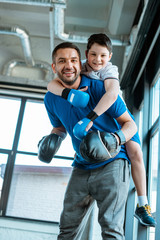 Wall Mural - father giving piggyback ride to happy son in boxing gloves at gym