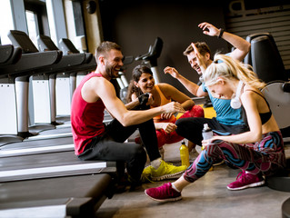 Wall Mural - Friends in sportswear talking and laughing together while sitting on the floor of a gym after a workout