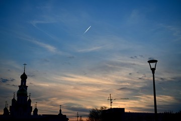  Silhouettes of an orthodox temple, construction cranes, houses and a lonely lantern. Against the sunset sky with clouds like brush strokes. And leaving the trace of the aircraft.