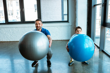 Canvas Print - father and son doing squats with fitness balls at gym