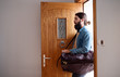Young hipster man with bag entering front door when coming back home.
