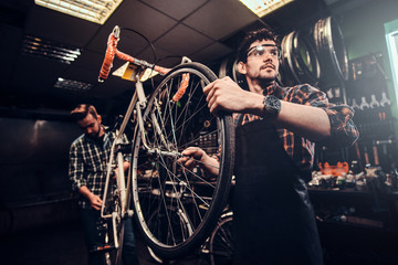 Wall Mural - Two attractive mans are working on bicycle fixing at busy workshop.