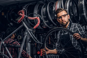 Wall Mural - Focused attractive man in glasses is chainging wheel for bicycle at busy workshop.