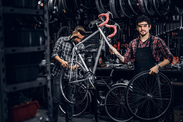 Wall Mural - Good teamwork of two nice mans at busy bicycle workshop. Mans are wearing checkered shirts.