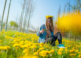 young beautiful girl enjoying nature in a field of beautiful yellow dandelions making summer selfie on the phone