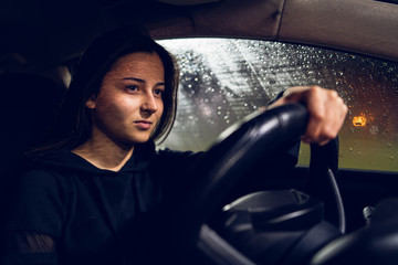 Young woman holding a car driving wheel in a rainy night rain