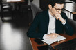 © Strelciuc - Portrait of a young confident manager thinking while drinking coffee and writing in his notebook while sitting in a coffee shop.