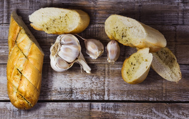 Baguette with garlic butter, aromatic herbs and slice of garlic on wood. Top view food photography