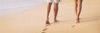 © Maridav - Beach couple walking barefoot on sand at sunset walk honeymoon travel banner - woman and man relaxing together leaving footprints in the sand.