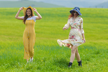 Two women in bright hats and clothes walking on a bright green meadow