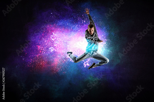 Modern female dancer jumping in hoodie with colourful splashes background. Mi...