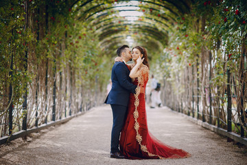 Beautiful woman in a long red dress walks around the city with her husband in a blue suit and with a beard