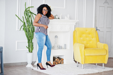 Beautiful african american woman with curly afro hair and eyeglasses posed in room.