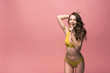 © LIGHTFIELD STUDIOS - smiling young woman in yellow swimsuit showing hush sign isolated on pink