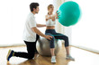 © nenetus - Physiotherapist helping patient to do exercise on fitness ball in physio room.