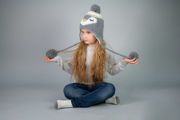 Beautiful smiling teenage girl with long hair in a winter hat - on gray-silver background