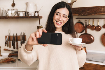 Wall Mural - Smiling young girl having cup of coffee at the kitchen