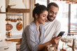 © Drobot Dean - Photo of smiling brunette couple drinking coffee and using cell phone during breakfast at home