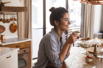 Canvas Print - Photo of happy brunette woman 20s drinking coffee while having breakfast at home