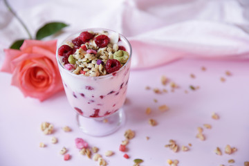 yogurt parfait with fresh raspberry berries and rose on a light pink background. Healthy food. With copy space for text.