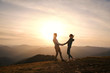 © vitaliymateha - Silhouette of loving couple standing on edge of mountain and holding hands on sunset sky and mountains background.