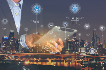 Smart city or Internet of Things (IoT), Double exposure of Businessman hands holding digital tablet with icon or hologram on city background, Communication network service and Business concept